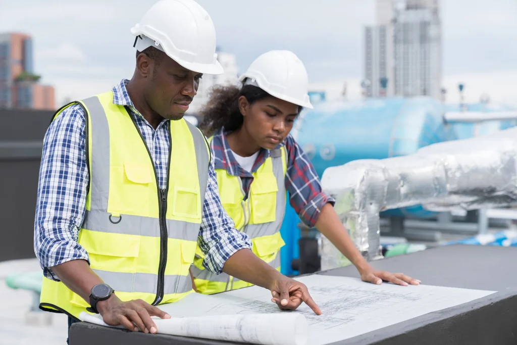 Man and woman in hard hats and high visibility vests looking at construction plans.